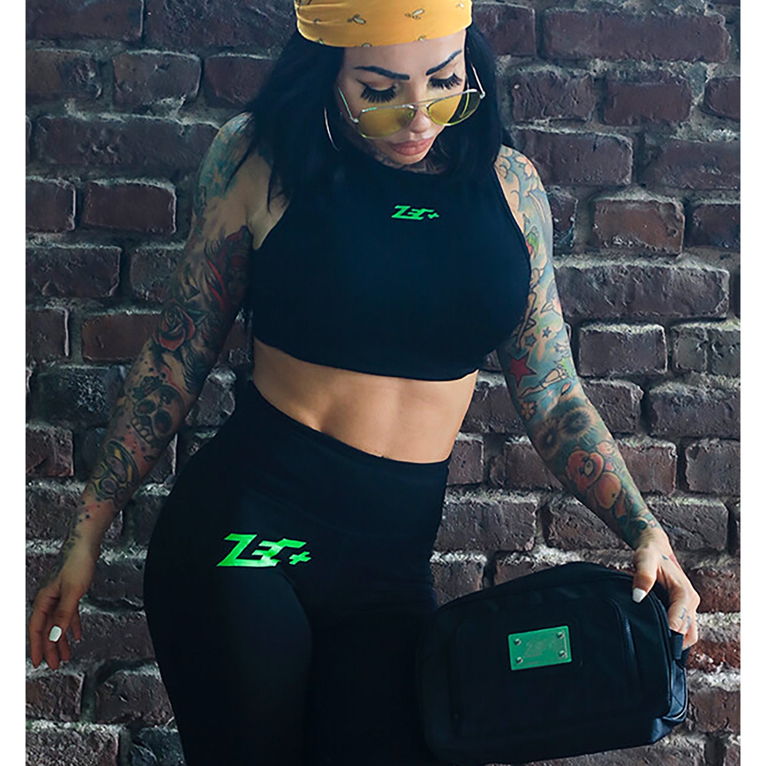 Zecplus Lifestyle Kulturbeutel Schwarz Frau mit Tattoos vor Ziegelsteinmauer hält den Kulturbeutel